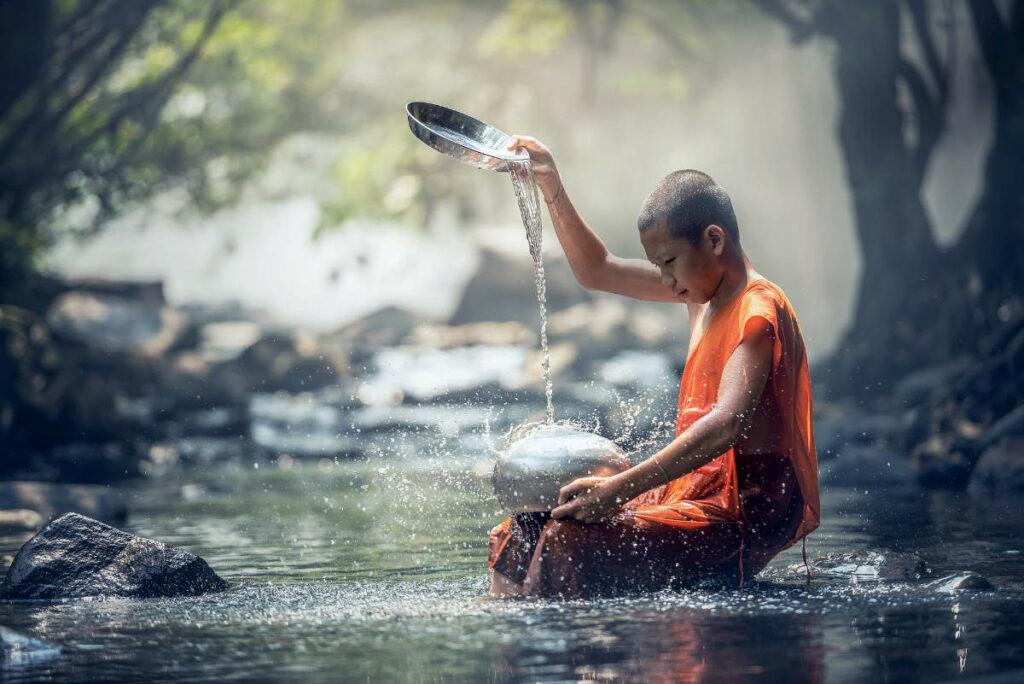 Boy monk pouring water, sitting in a river. Photo by sasint from Pixabay https://pixabay.com/images/id-1807518/